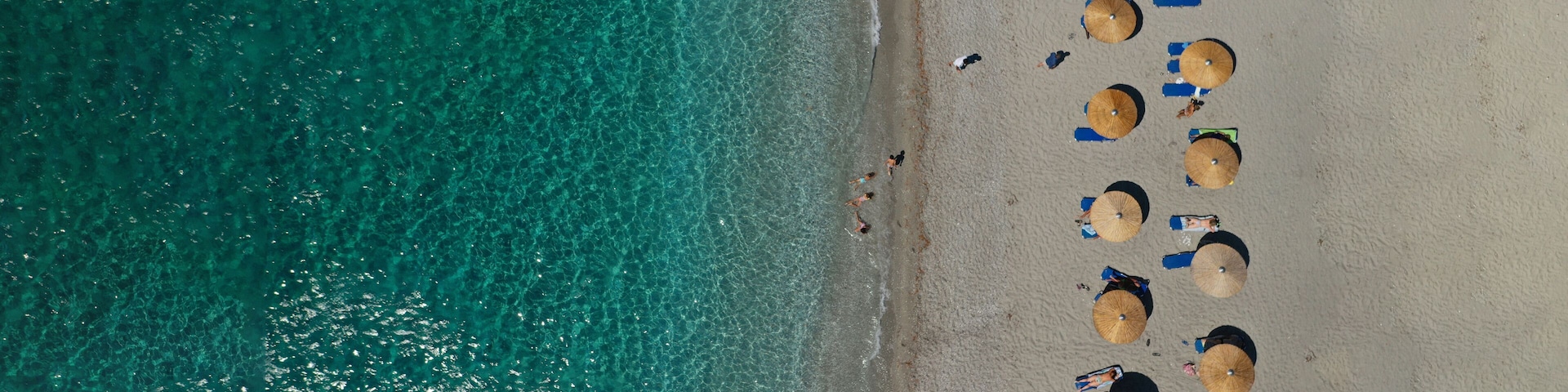 Vista aérea de una playa con agua turquesa cristalina, varias sombrillas y gente tomando el sol.