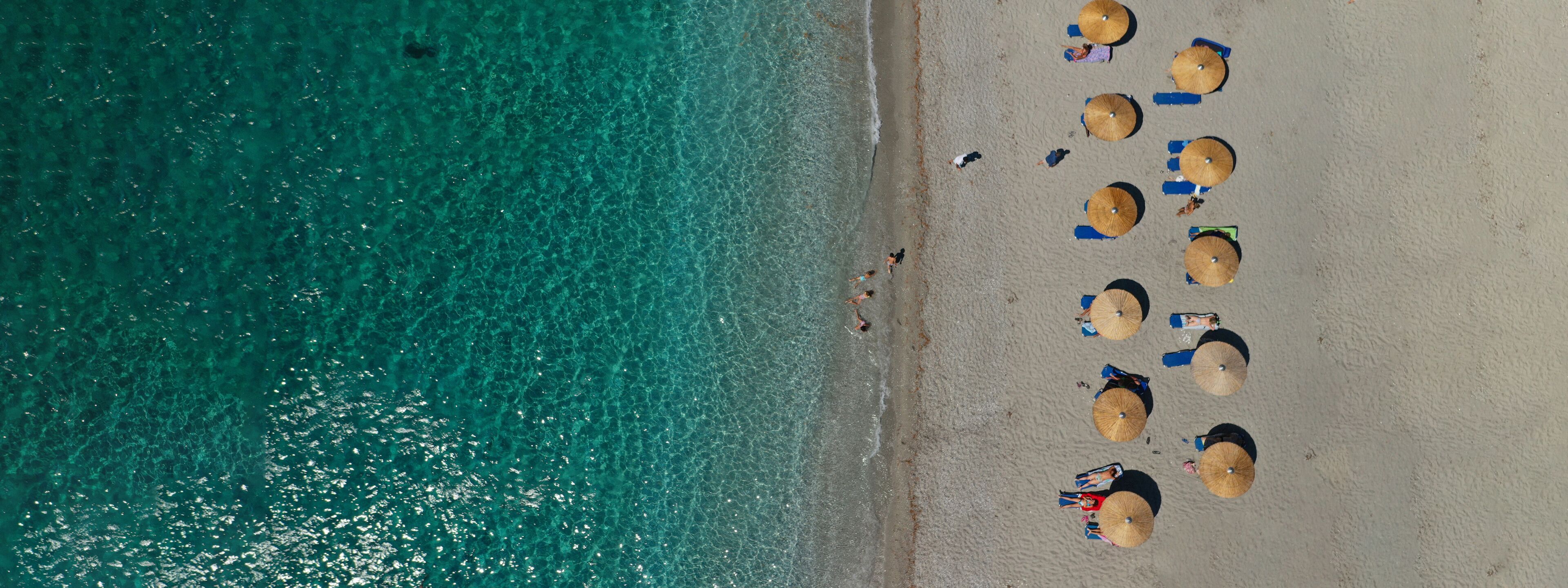 A beach with clear turquoise water, several umbrellas, and people sunbathing.