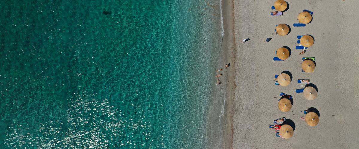 A beach with clear turquoise water, several umbrellas, and people sunbathing.