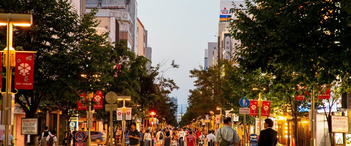A busy urban street lined with trees and various shops.