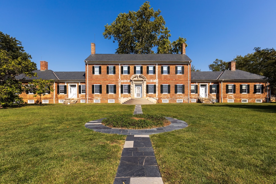 A large brick building with a central entrance, surrounded by a well-maintained lawn and a circular stone pathway.