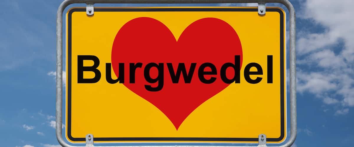 A sign with a heart and the word "Burgwedel" against a blue sky with clouds.
