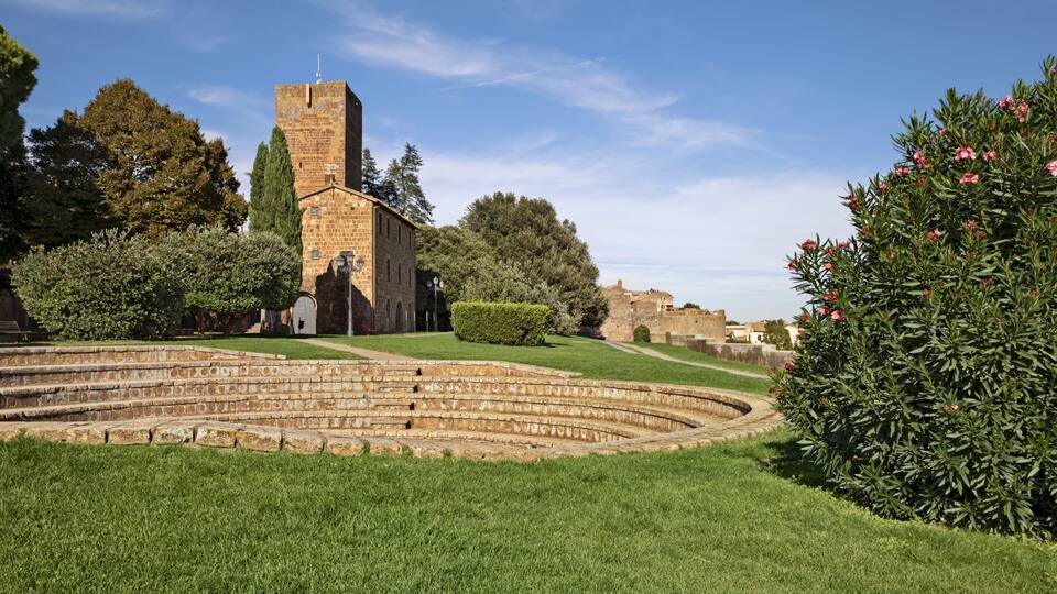 A historic stone building with a tower, surrounded by well-maintained grass and trees.