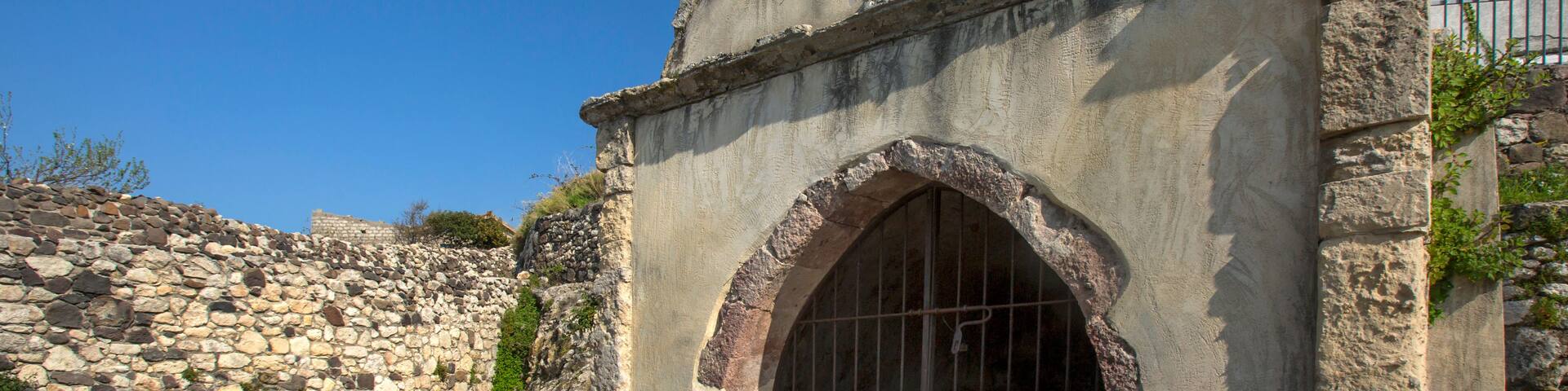 A stone church with a cross, arched entrance, and a stone wall in the background.