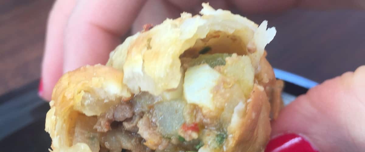 A hand holding a half-eaten stuffed pastry with visible meat and vegetables.