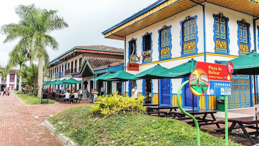 A colorful building with blue and yellow accents, a palm tree, and outdoor seating areas.