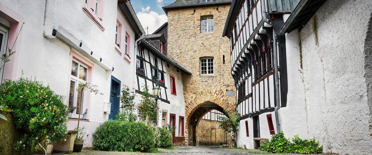 A narrow cobblestone street flanked by traditional half-timbered houses with a stone tower in the center.