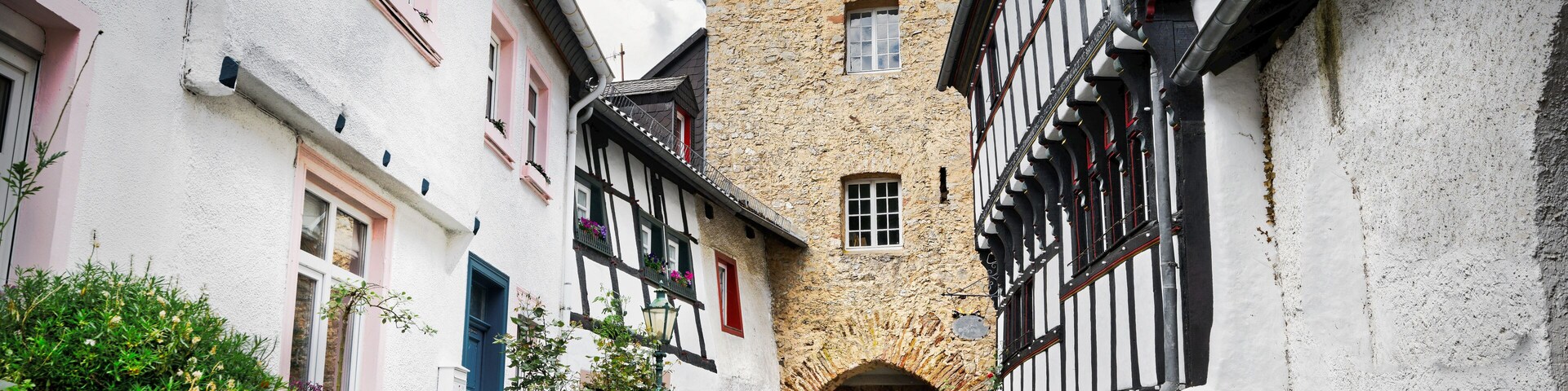 A narrow cobblestone street flanked by traditional half-timbered houses with a stone tower in the center.