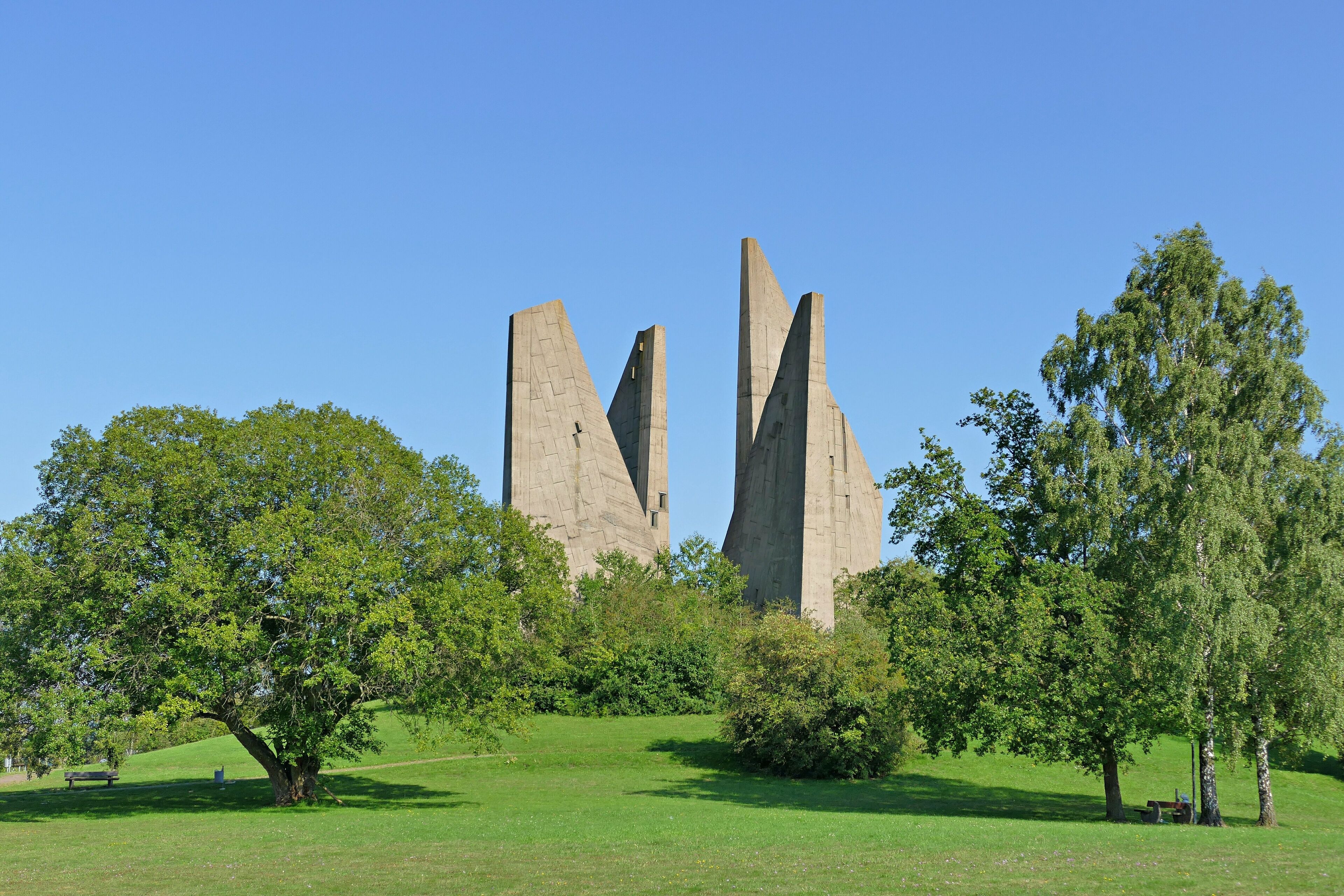 A park with three tall, pointed stone structures surrounded by lush green trees and grass.