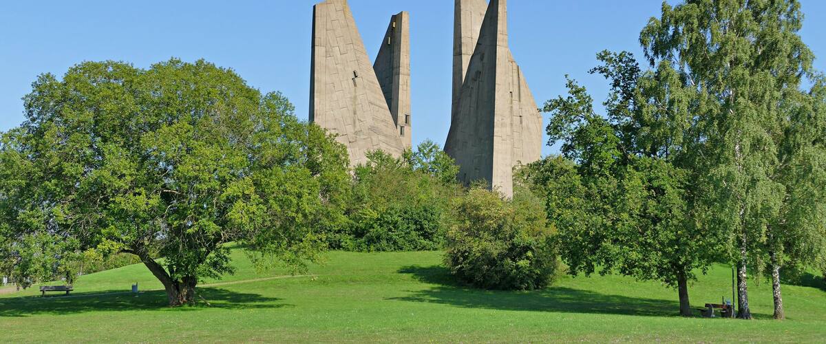 A park with three tall, pointed stone structures surrounded by lush green trees and grass.