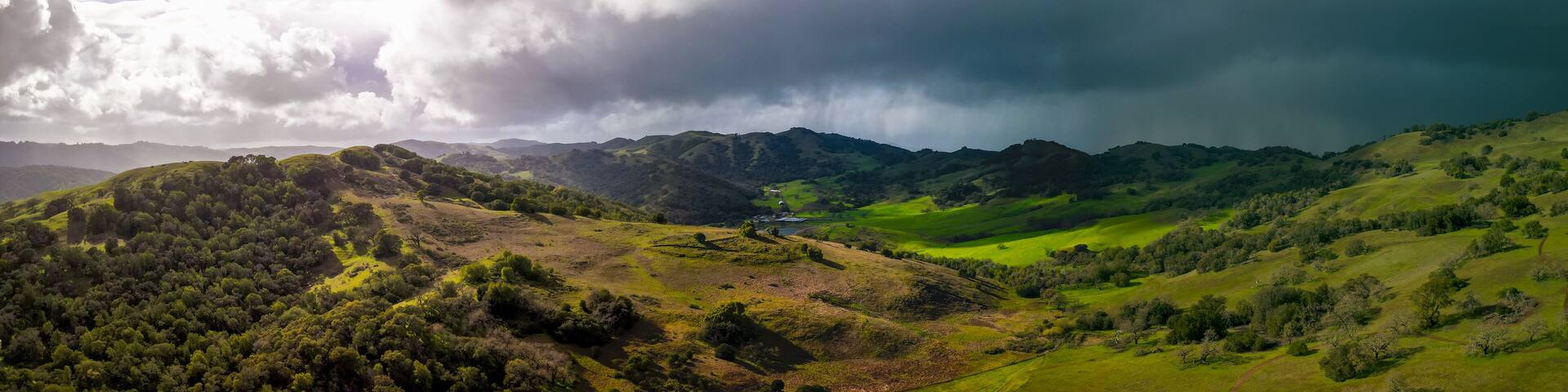 Panoramic view of bright sun and dark storm clouds over green California landscape