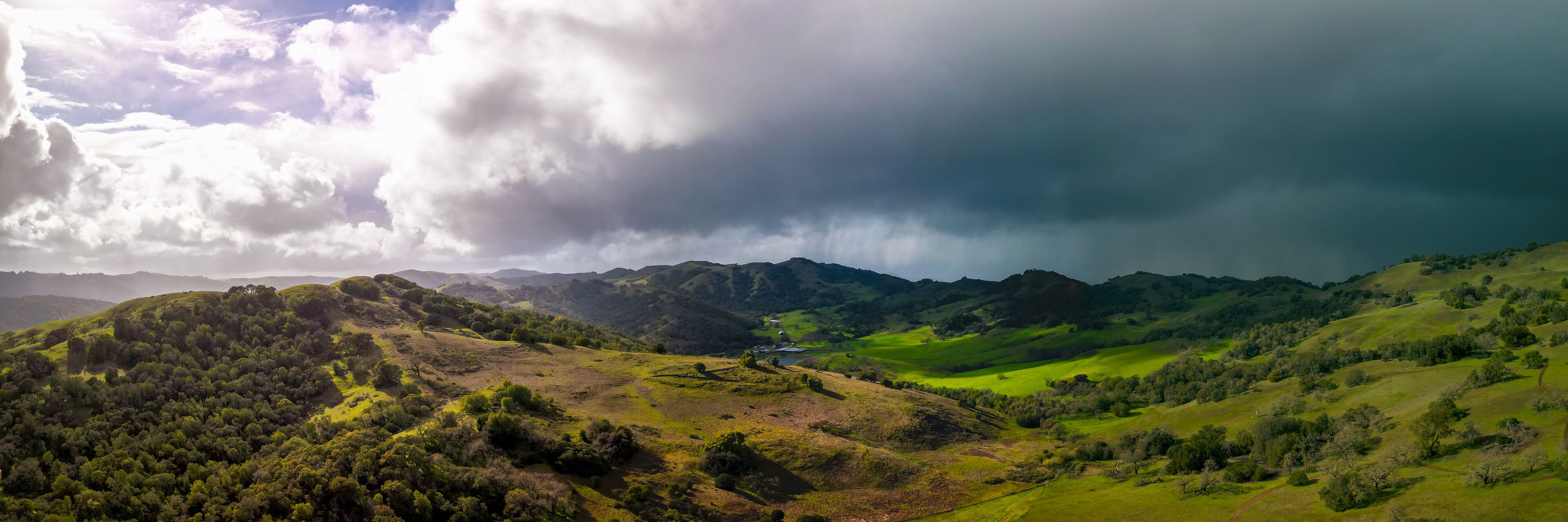 A lush green valley with rolling hills and a small house in the distance.