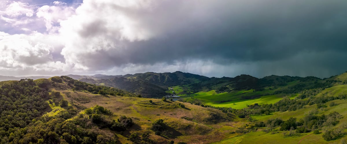 A lush green valley with rolling hills and a small house in the distance.