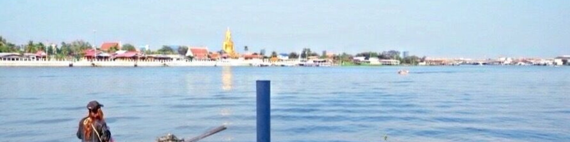 Um rio calmo com um pescador, um barco atracado no cais e um templo dourado ao longe.