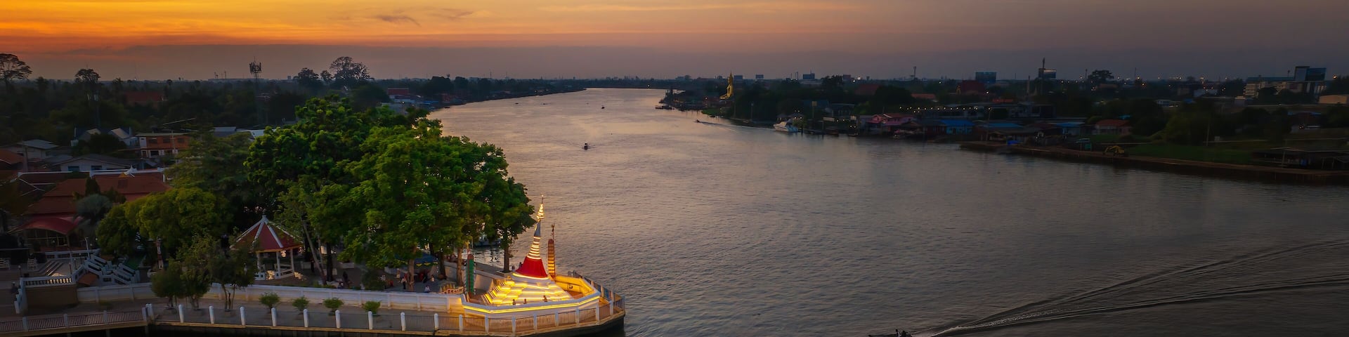 A river with a bridge, a dock with a boat, and a cityscape in the background.