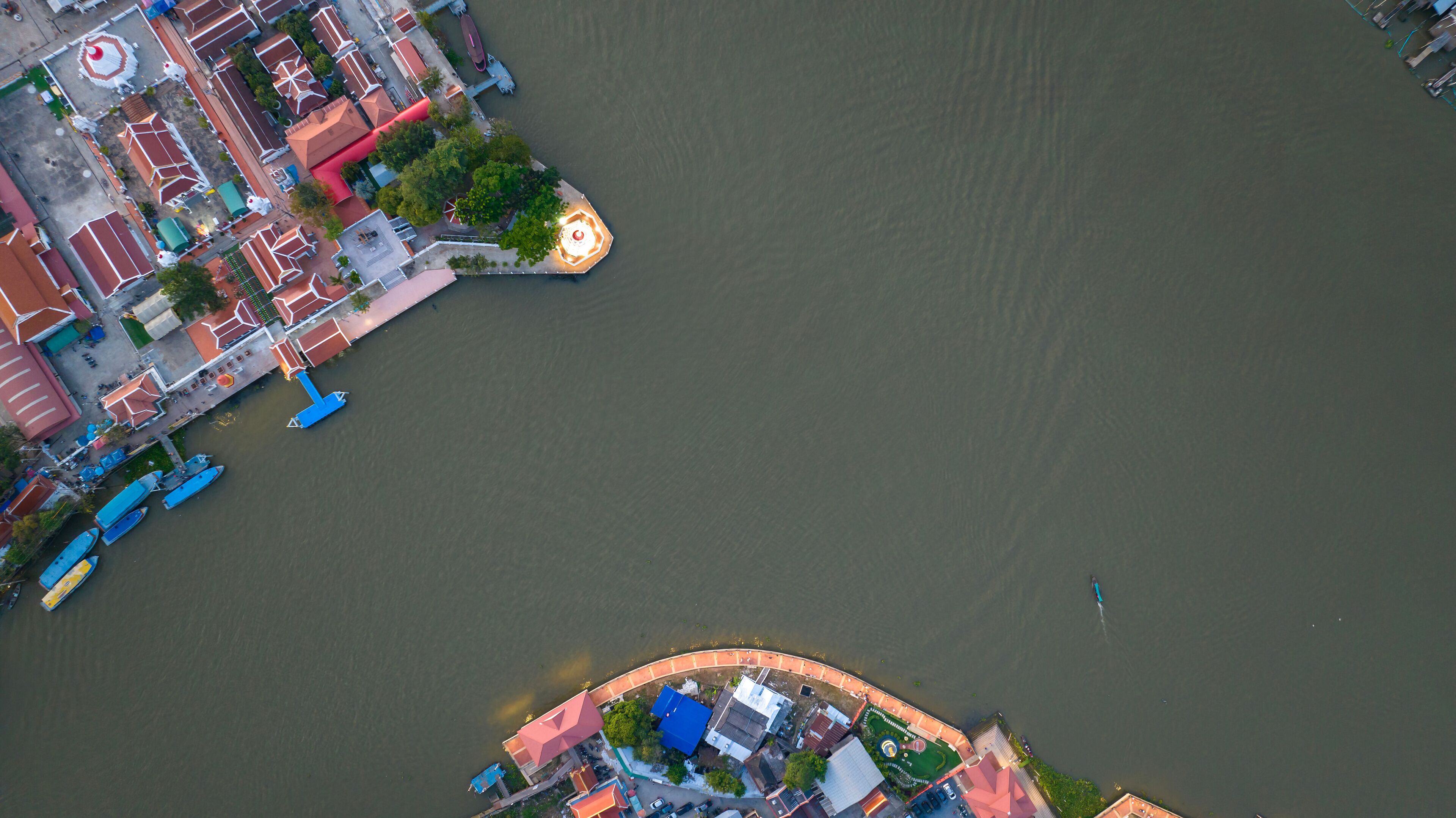 An aerial view of a riverside area with buildings, boats, and a circular structure near the water.