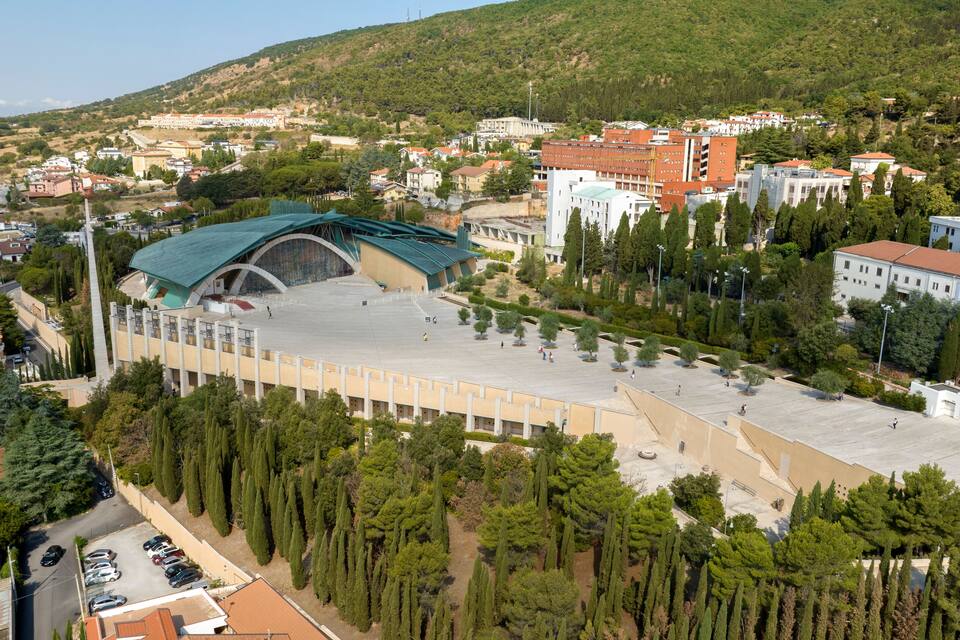 A large open plaza with a modern building featuring a green roof, surrounded by trees and residential buildings.
