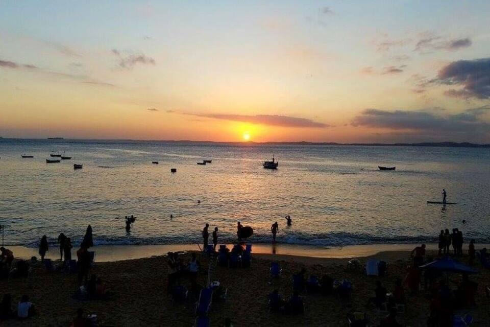 Una spiaggia al tramonto con barche sull'acqua e persone sulla riva.