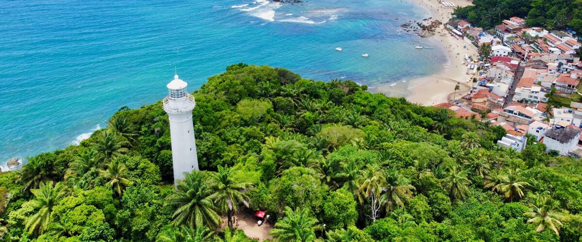 A coastal town with a lighthouse, beach, and dense greenery.