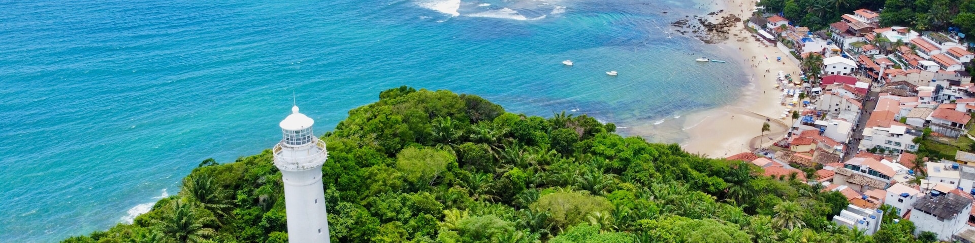 A coastal town with a lighthouse, beach, and dense greenery.