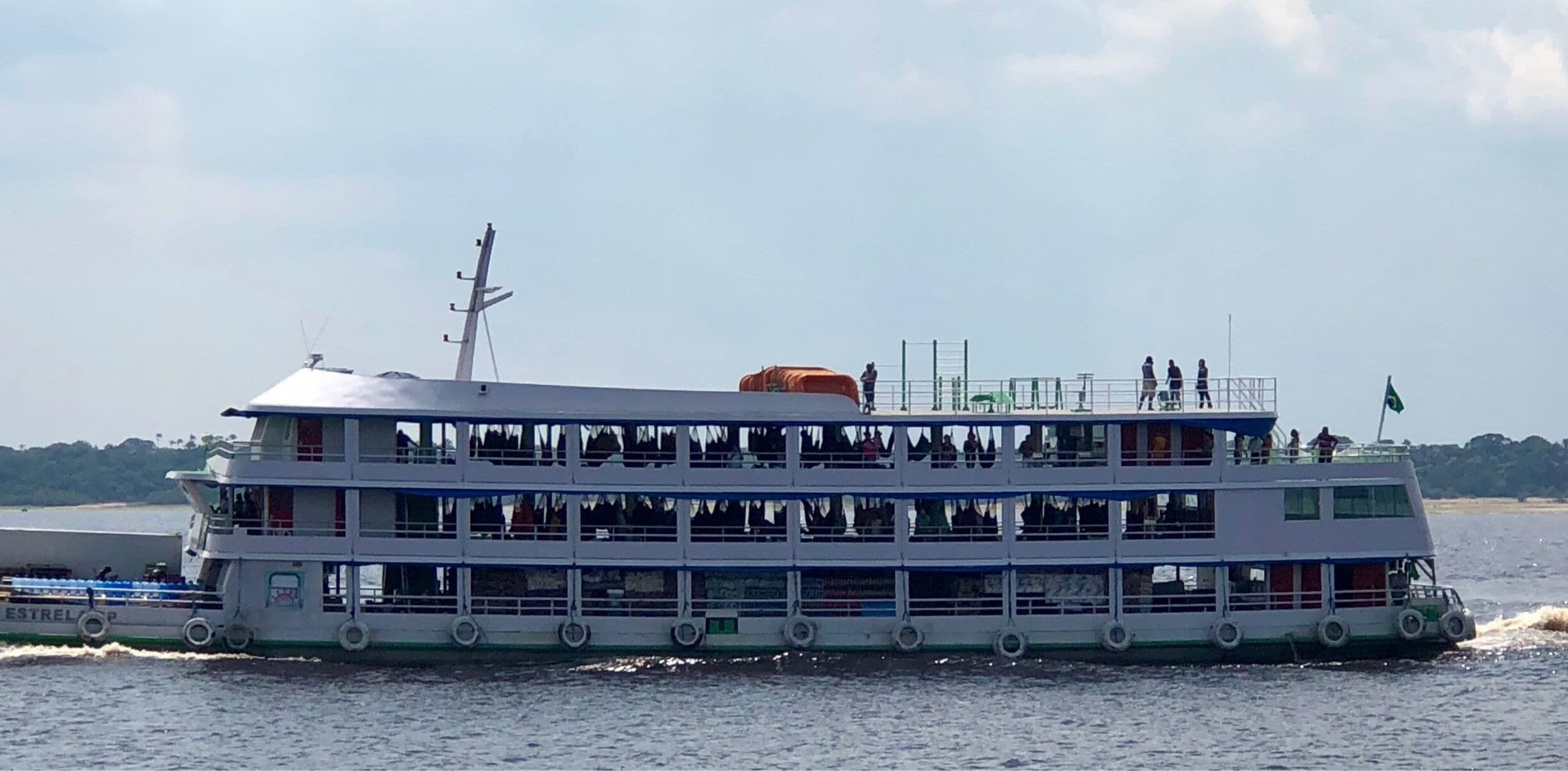 A fully loaded transportation ship heading down river.  If you look closely you can see cargo on the lower floor and hammocks containing passengers on the second floor.