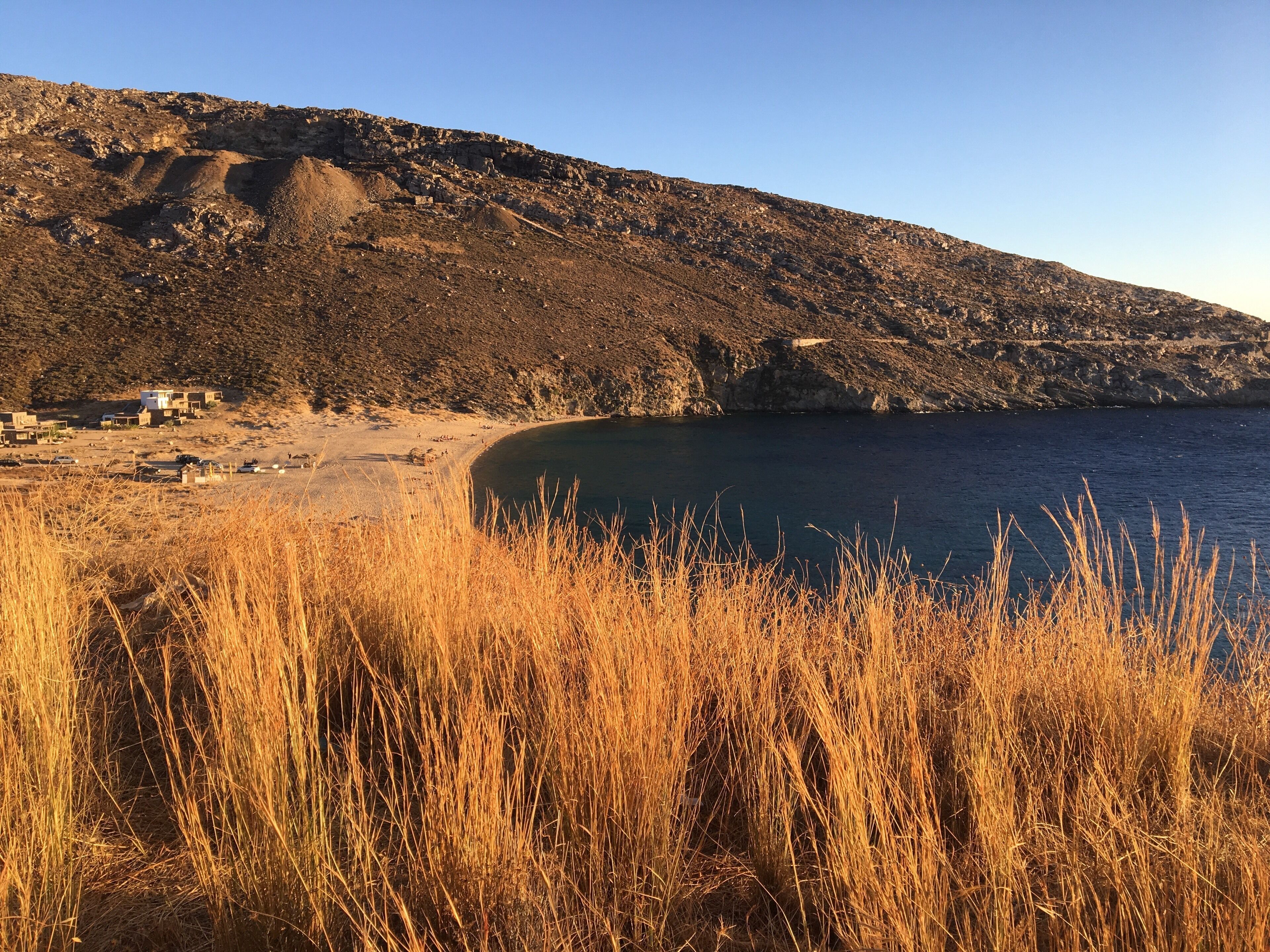 A coastal landscape with a rocky hillside, a sandy beach, and a clear blue sky.