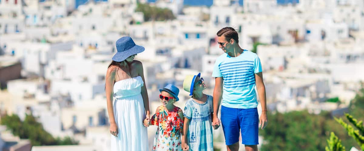 A family standing by a swimming pool with a white-washed town in the background.