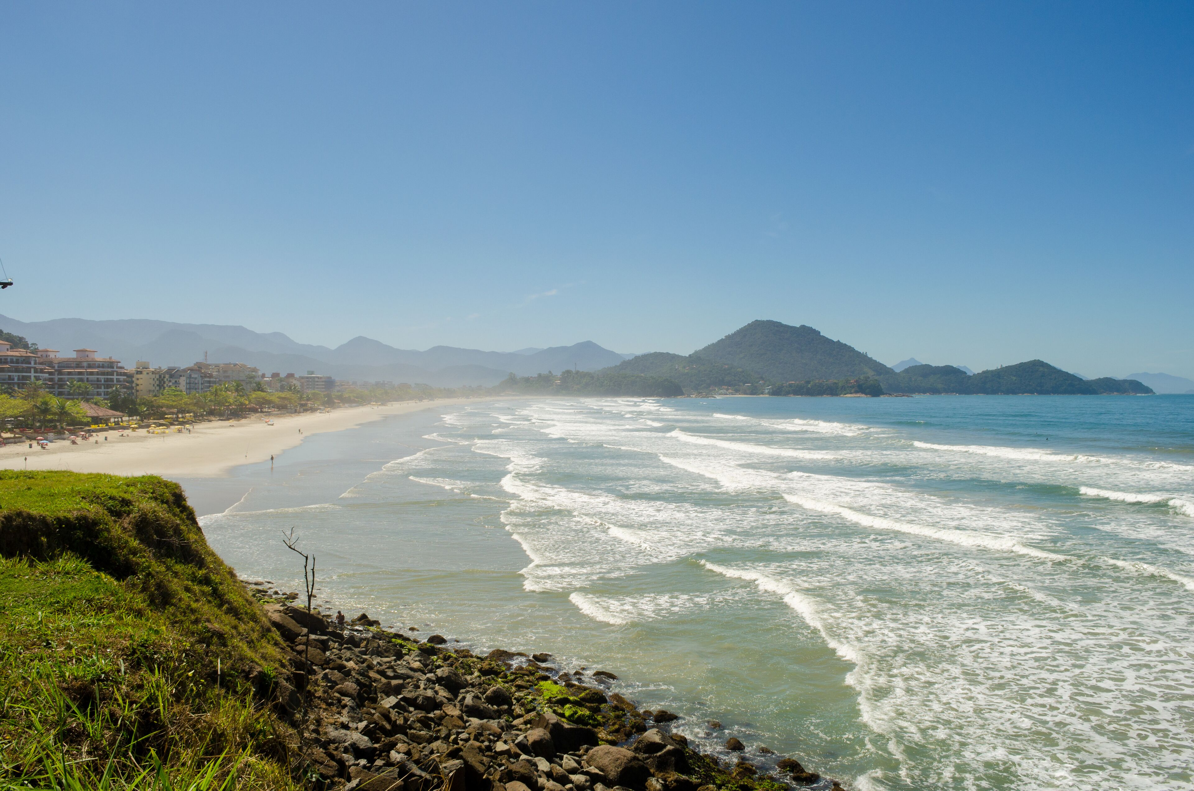 A beach with waves, a rocky shoreline, and mountains in the background.