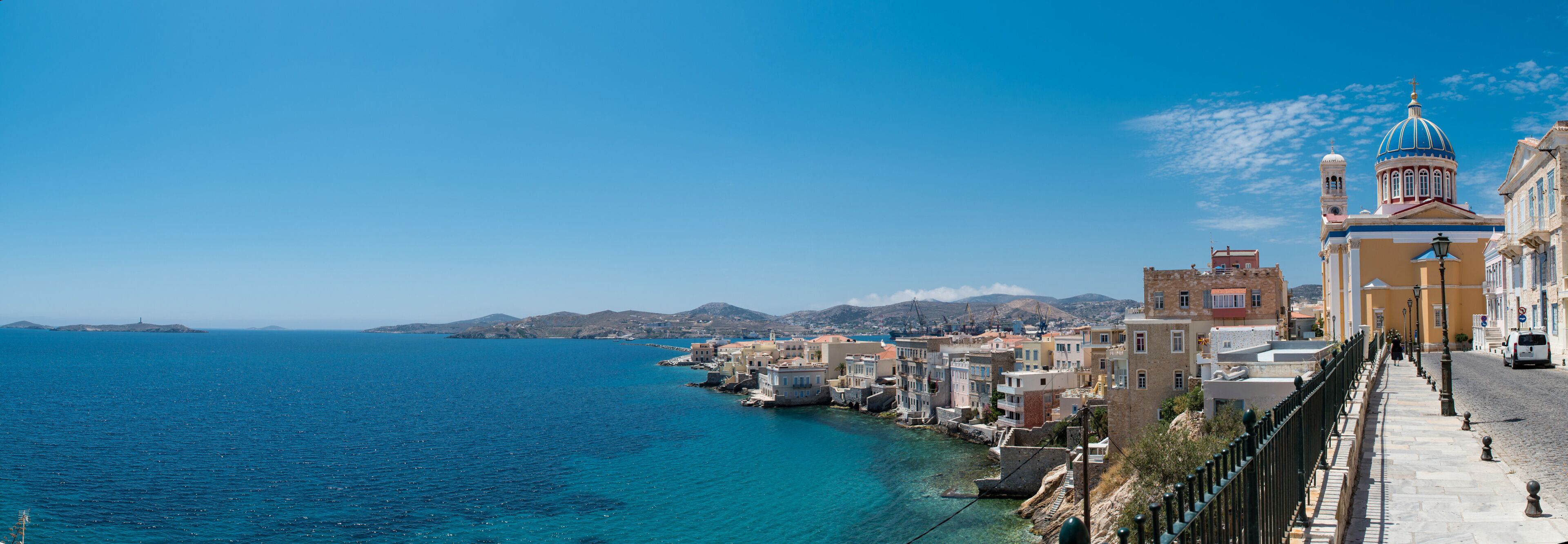 A coastal town with colorful buildings, a prominent church with a blue dome, and a clear blue sea.