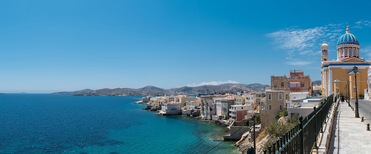 A coastal town with colorful buildings, a prominent church with a blue dome, and a clear blue sea.