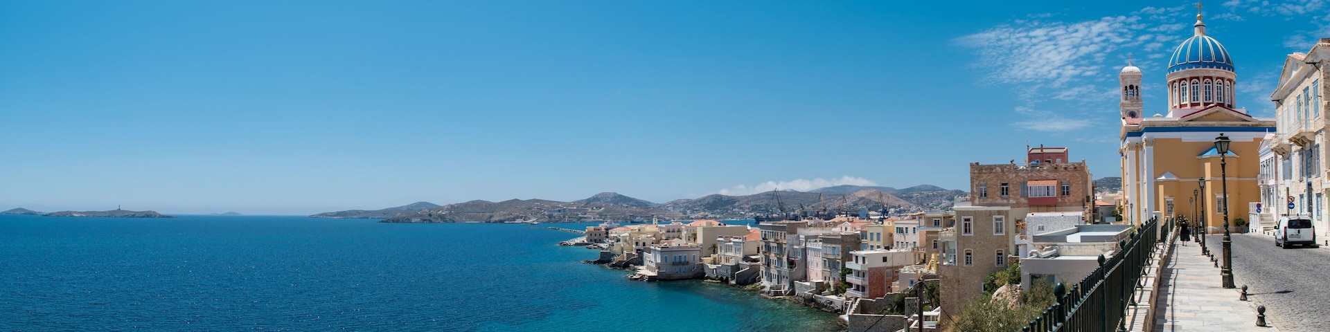 A coastal town with colorful buildings, a prominent church with a blue dome, and a clear blue sea.