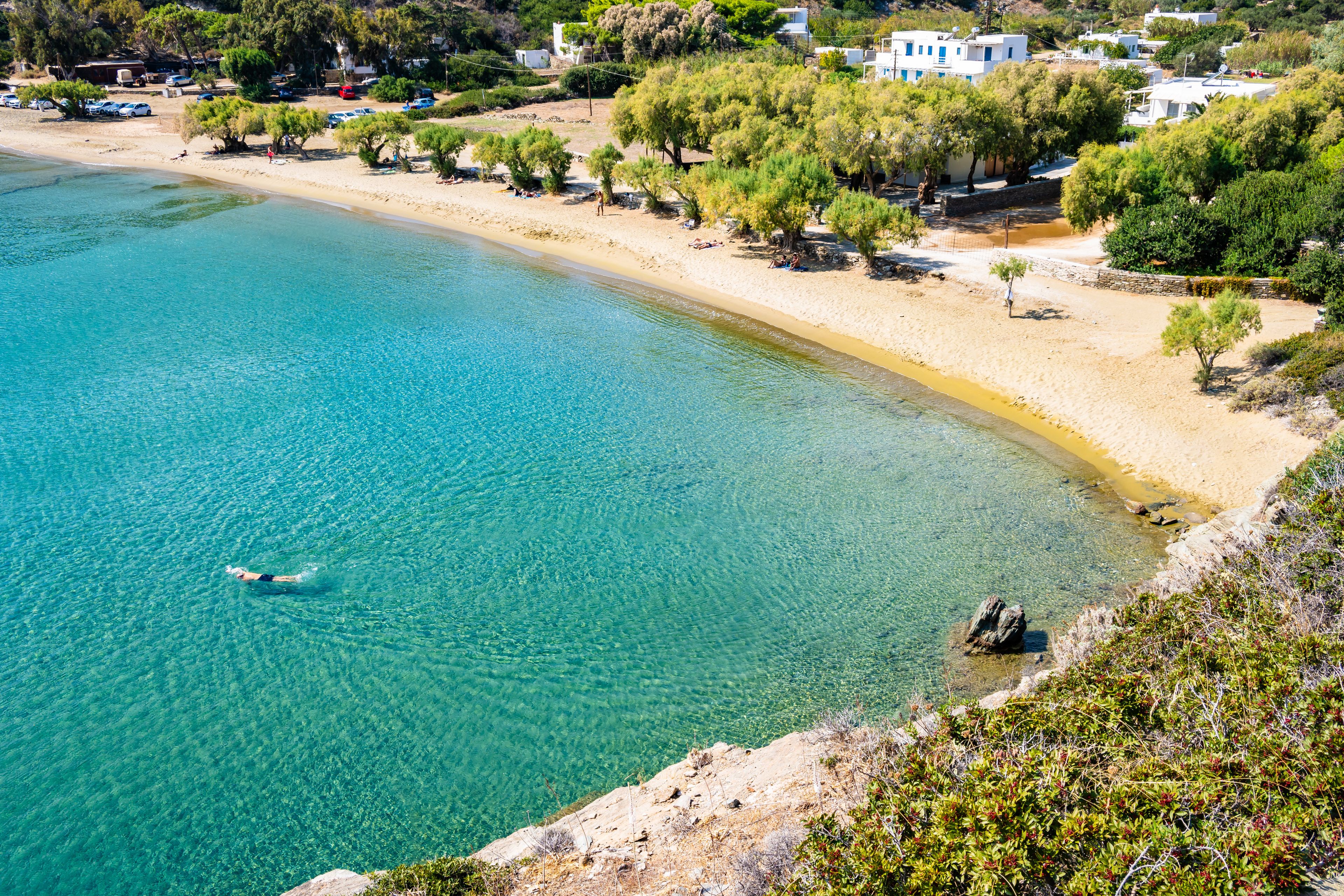 A coastal beach with clear turquoise water, a sandy shore, and a row of white buildings with blue accents.