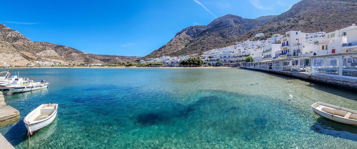 A coastal town with clear turquoise waters, boats docked at the pier, and white buildings with blue accents.
