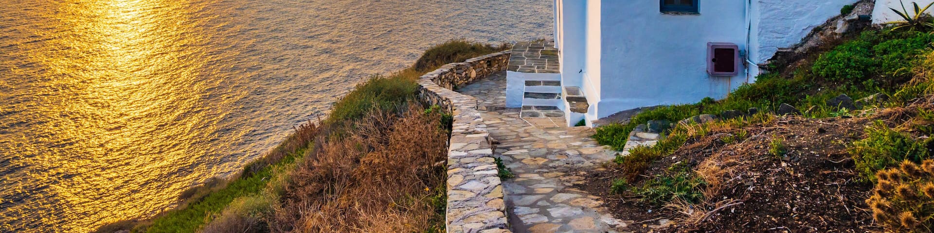 Sunrise over rocky coast of Sifnos island with typical white houses in foreground in Kastro village, Cyclades, Greece