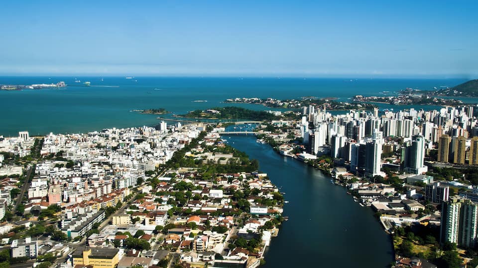 A coastal cityscape with a river running through it, surrounded by high-rise buildings and a clear blue sky.