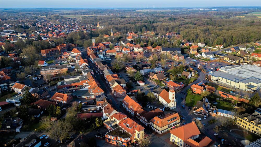 Eine Vogelperspektive auf eine Stadt mit roten Dächern, einem markanten Kirchturm und einem großen Industriegebäude.