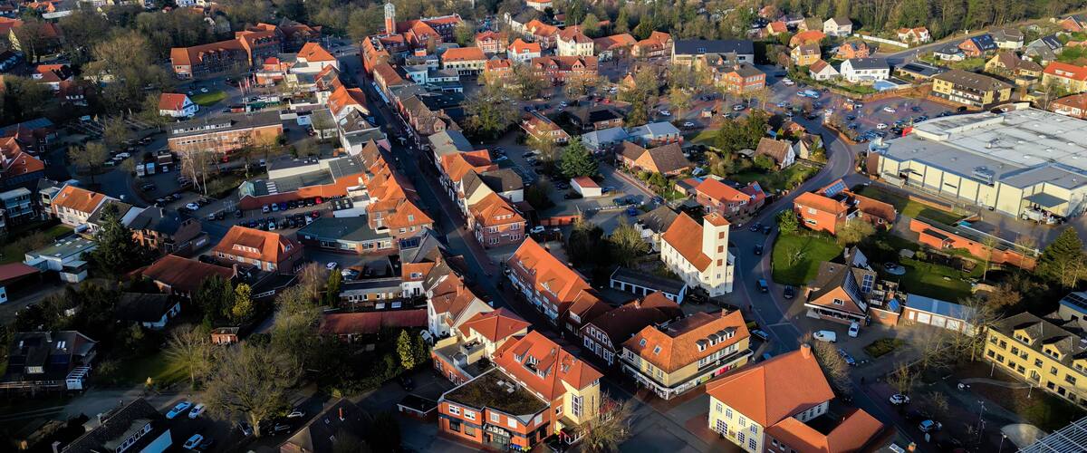 An aerial view of a town with red-roofed houses, a prominent church tower, and a large industrial building.