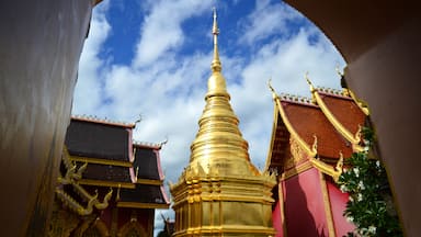 Um stupa dourado com um pináculo, cercado por arquitetura tailandesa tradicional com telhados e decorações elaboradas.