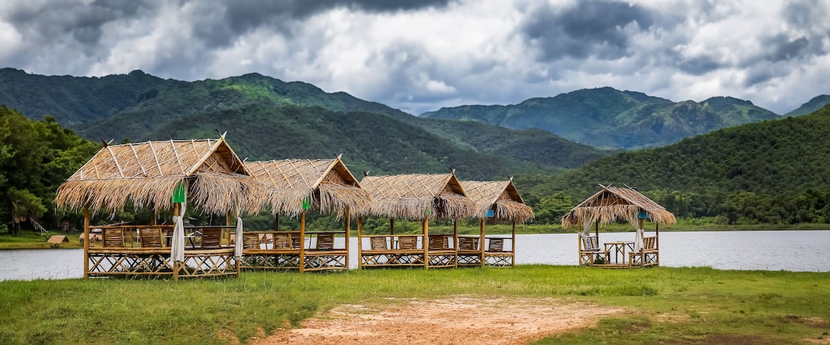 Thatched-roof huts by a lake with mountains in the background.