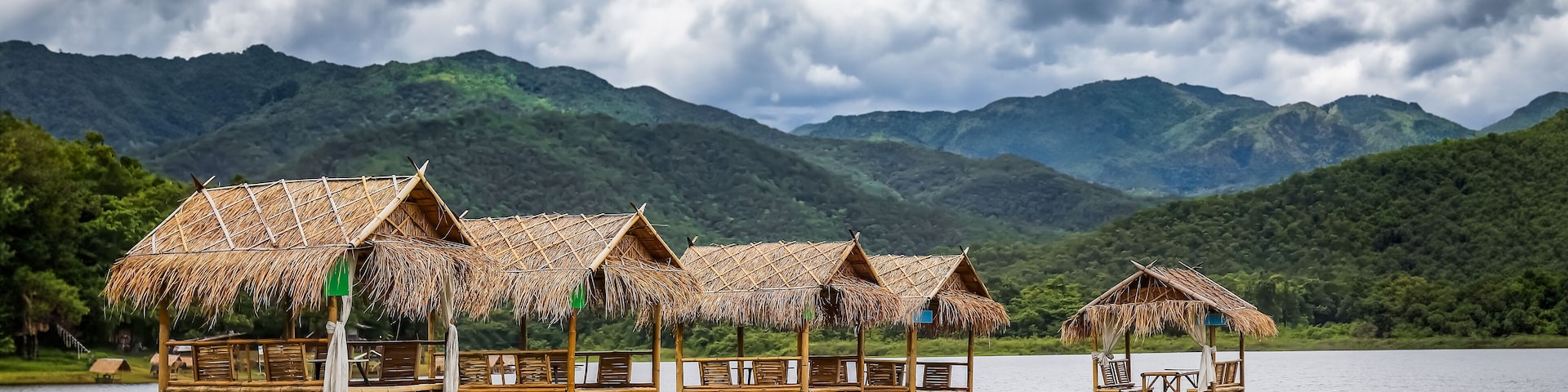 Thatched-roof huts by a lake with mountains in the background.