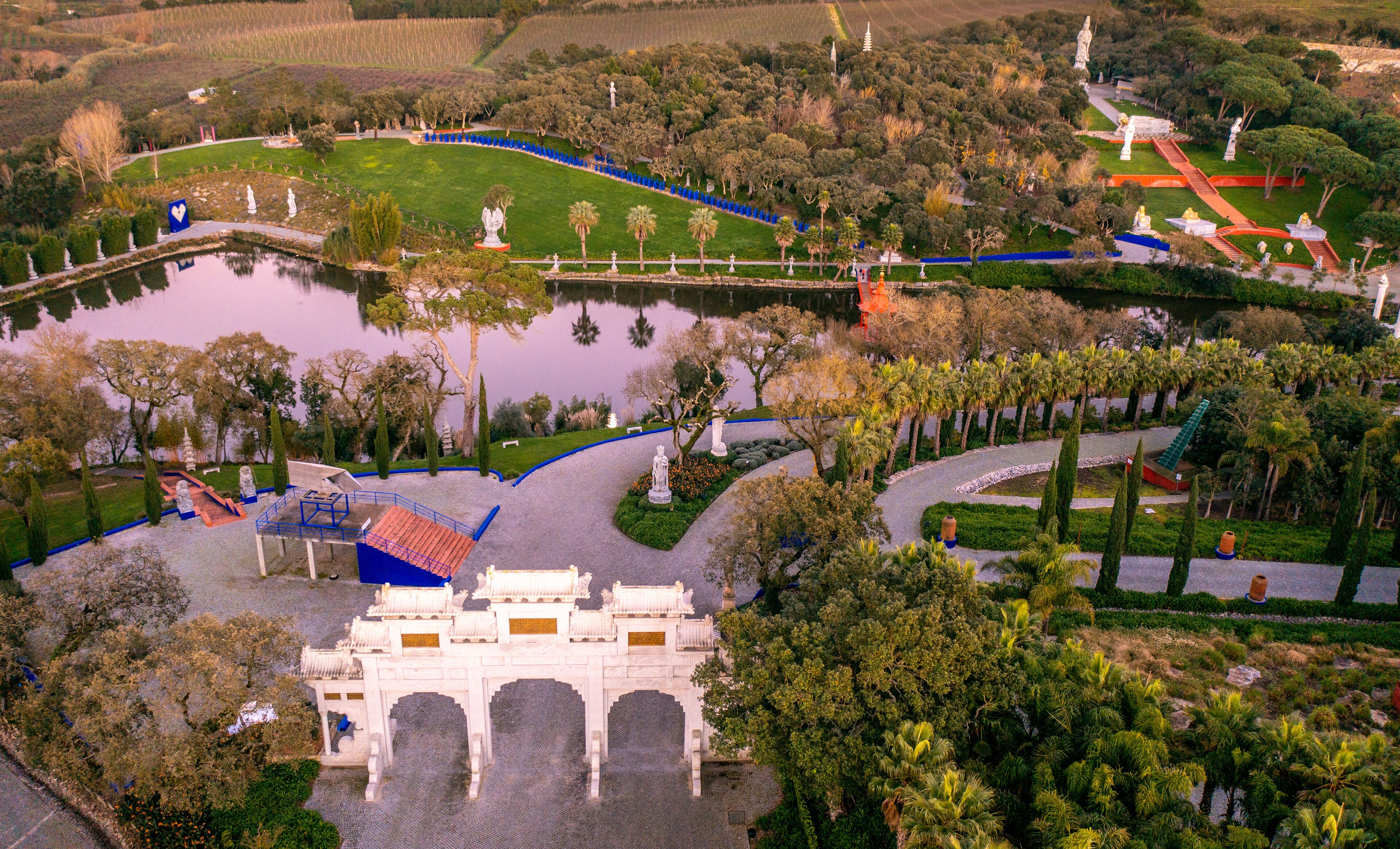 An aerial view of a park with a large pond, statues, and a traditional gate.