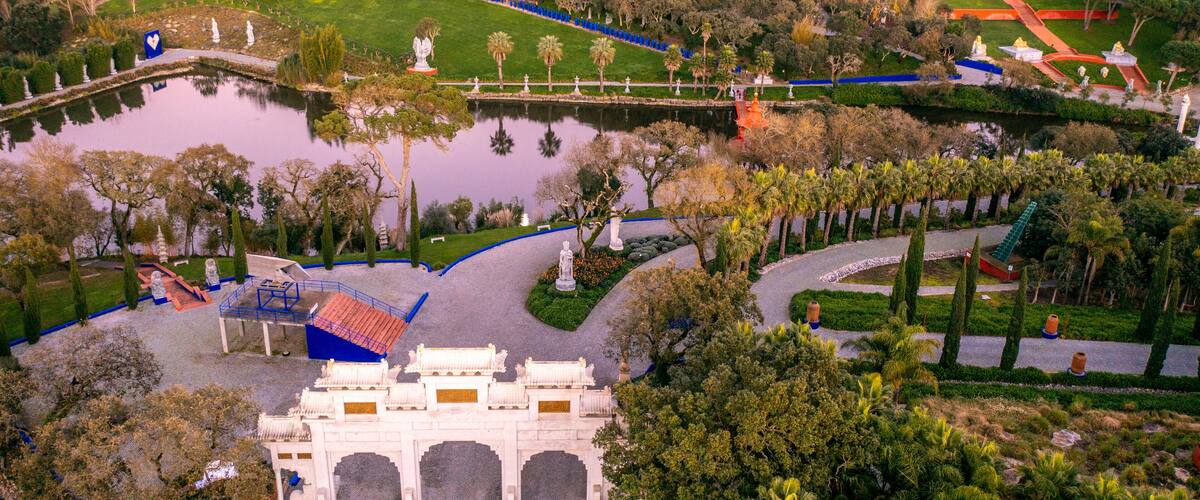 An aerial view of a park with a large pond, statues, and a traditional gate.