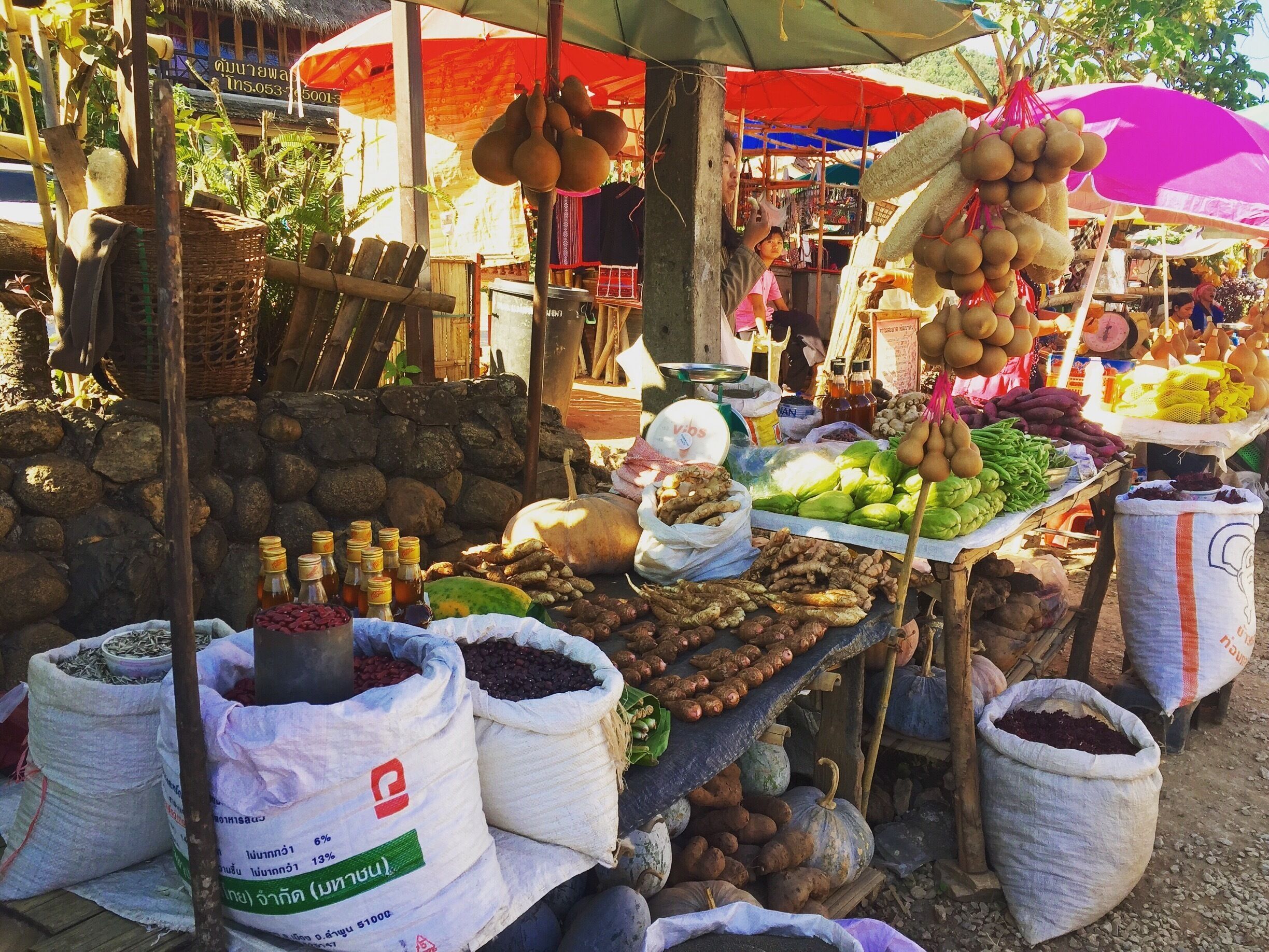 A market stall with various vegetables, fruits, and sacks of produce.
