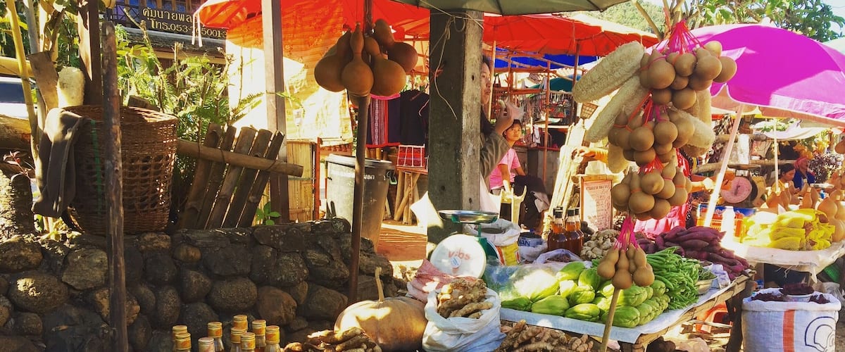 A market stall with various vegetables, fruits, and sacks of produce.