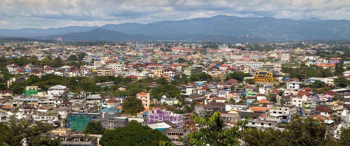 A densely populated cityscape with colorful buildings, a river, and mountains in the background.