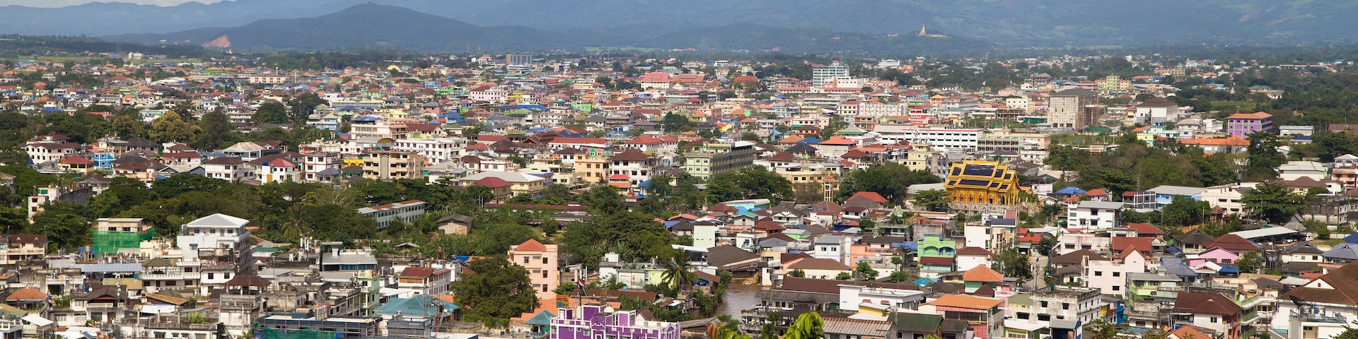 A densely populated cityscape with colorful buildings, a river, and mountains in the background.