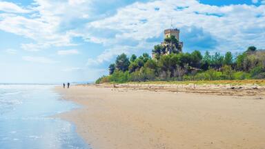 A beach with a tower on a hill, people walking, and a clear sky.