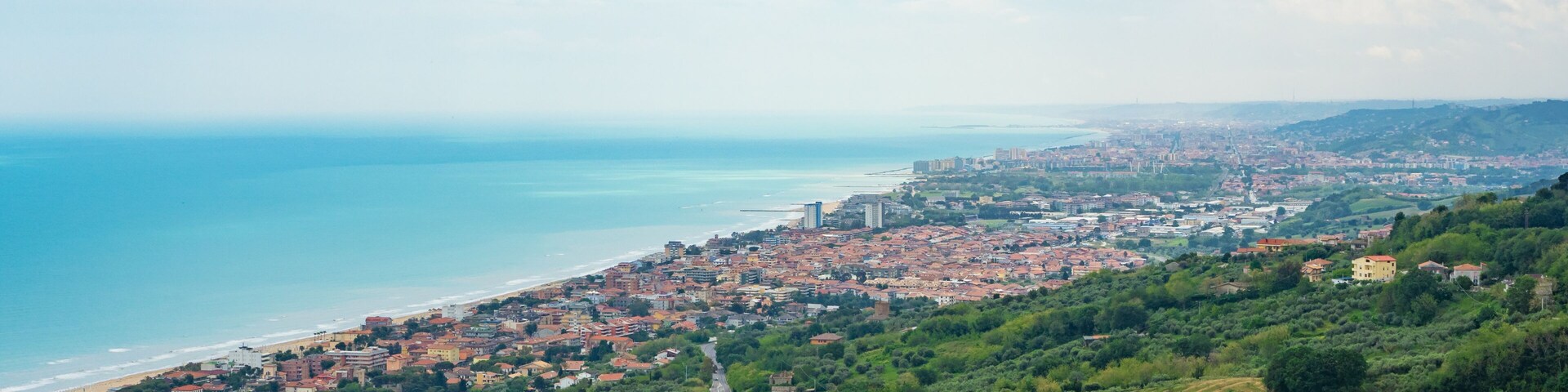 Una ciudad costera con zonas urbanas y rurales, un camino sinuoso y vistas al mar.