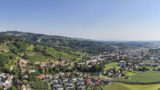 Aerial view of the verdant landscape with the scattered red-roofed buildings and the distant silhouette of a monastery on the hill, Deutschlandsberg, Styria, Austria.