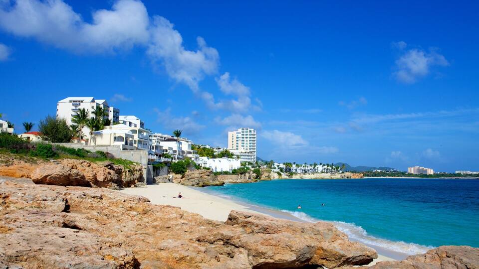 A coastal town with white buildings, a beach, and clear blue waters.